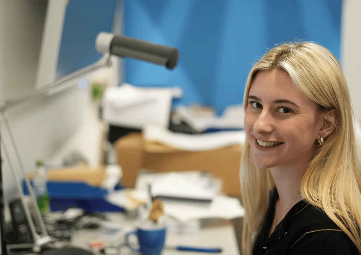 Mitarbeiterin sitzt im Büro und lächelt in die Kamera.